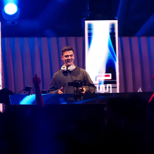 Nimino DJ set at the Sunset event in Hangar-7 – the artist smiles behind the deck in front of a blue-illuminated background and a celebrating crowd.